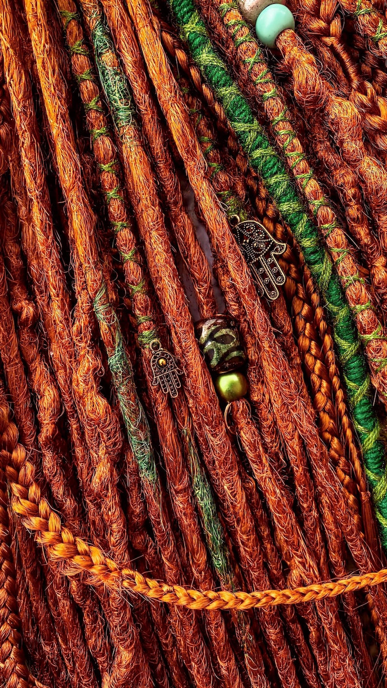 a close-up view of a collection of braided hair strands in various colors, including orange, green, and brown, with some beads and charms attached.