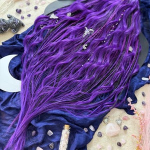 a long, vibrant purple wig with intricate braids and various crystals and gemstones scattered around it, creating a mystical and enchanting atmosphere.