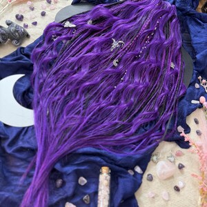 a long, vibrant purple wig with intricate braids and various crystals and gemstones scattered around it, creating a mystical and enchanting atmosphere.