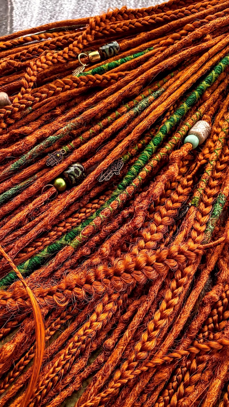 a close-up view of a collection of braided hair strands in various shades of orange and green, with some beads or accessories attached to the braids.