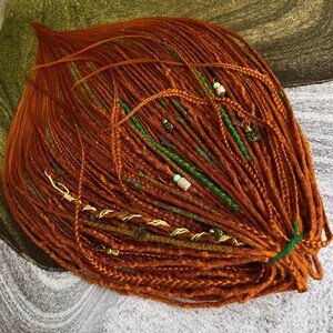 a large bundle of braided hair in various shades of orange, with green and white beads mixed in.