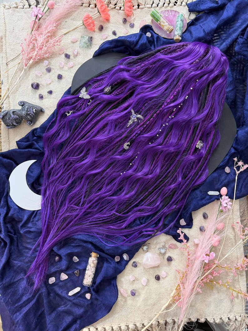 a purple wig with long, wavy hair, surrounded by various objects such as crystals, flowers, and a crescent moon.