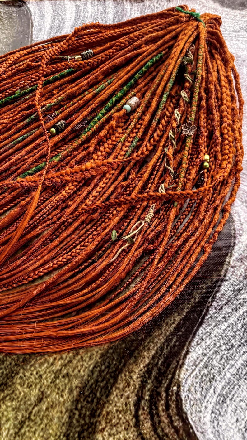 a close-up view of a large pile of braided orange hair, with various green and silver beads and accessories attached to the braids.