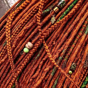 a close-up view of a collection of braided hair strands, with some of the braids adorned with beads and charms. The colors of the braids and the beads are predominantly orange and green, creating a vibrant and eye-catching display.