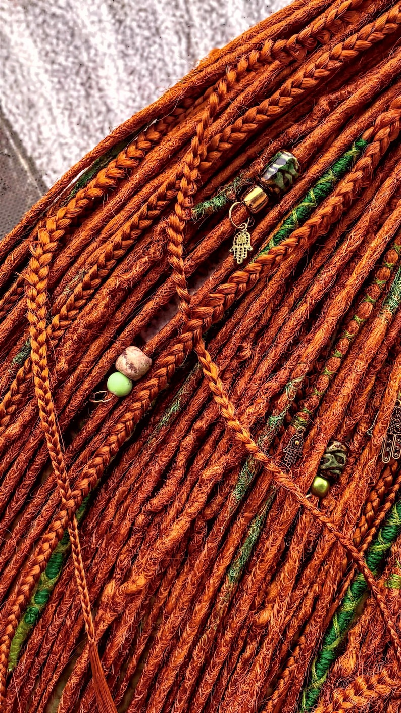 a close-up view of a collection of braided hair strands, with some of the braids adorned with beads and charms. The colors of the braids and the beads are predominantly orange and green, creating a vibrant and eye-catching display.