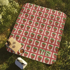May include: A red and white picnic blanket with a strawberry pattern. The blanket has the initials "TS" in green letters in the center.