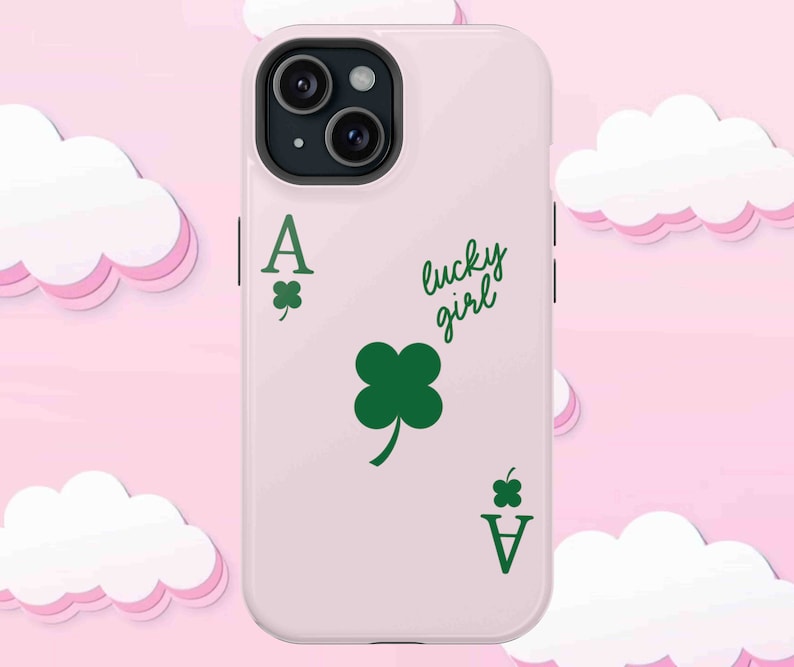 May include: A light pink phone case featuring a green Ace of Clubs card design with a four-leaf clover and the words "lucky girl" in a script font. The case has a black camera lens.