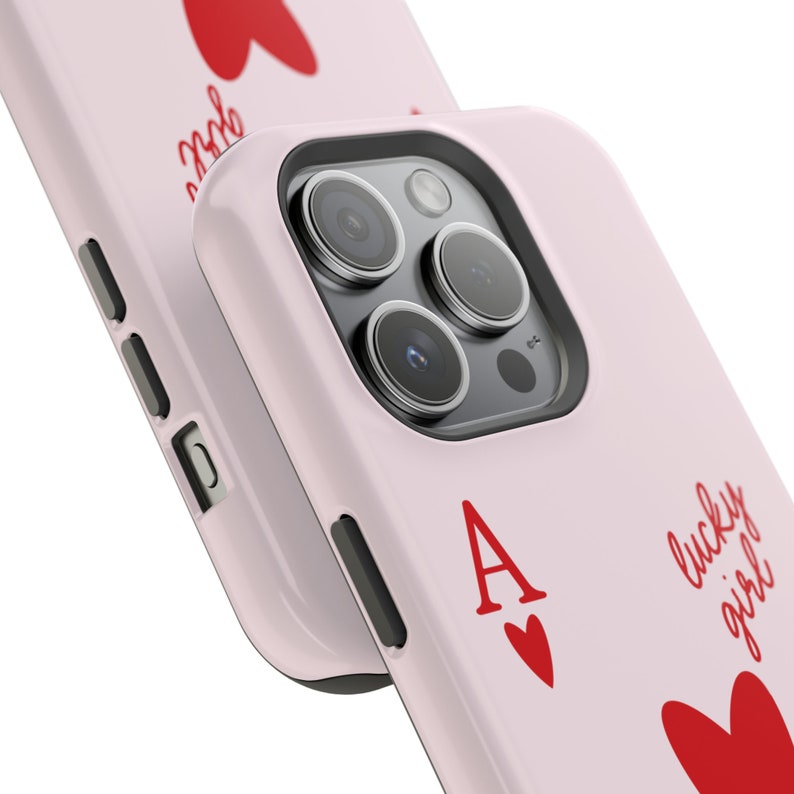 May include: A pink phone case with a red ace of hearts playing card design. The case has a cutout for the camera lens and a raised edge around the screen. The text "lucky girl" is written on the case in red.