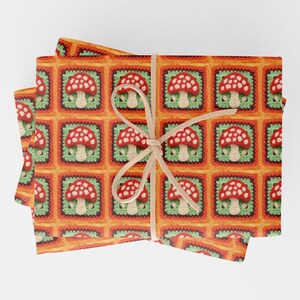 May include: A stack of orange and green wrapping paper with a crocheted mushroom pattern. The paper is tied with a beige ribbon.