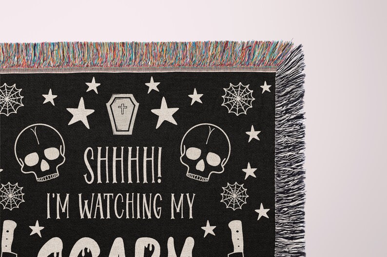 K&ouml;nnte beinhalten: Schwarze gewebte Wurfdecke mit einem gruseligen Halloween-Design. Sie zeigt zwei wei&szlig;e Sch&auml;del, einen Sarg, Spinnweben, Sterne und den Text "Psst! Ich beobachte mein gruseliges..."