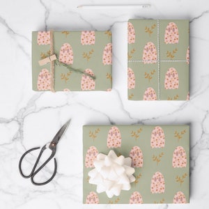 Pode incluir: Tr&ecirc;s caixas de presente embrulhadas em papel de embrulho verde com um padr&atilde;o de fantasma floral rosa e marrom. As caixas est&atilde;o sobre uma superf&iacute;cie de m&aacute;rmore branco com uma tesoura e um l&aacute;pis.