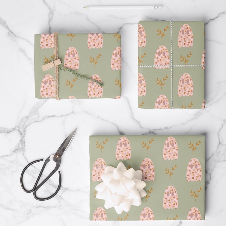 Pode incluir: Tr&ecirc;s caixas de presente embrulhadas em papel de embrulho verde com um padr&atilde;o de fantasma floral rosa e marrom. As caixas est&atilde;o sobre uma superf&iacute;cie de m&aacute;rmore branco com uma tesoura e um l&aacute;pis.
