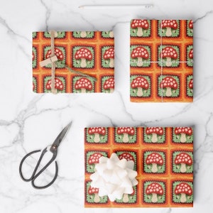May include: Gift wrap featuring a repeating pattern of red and white mushrooms in green and orange squares. The pattern resembles a crocheted design.