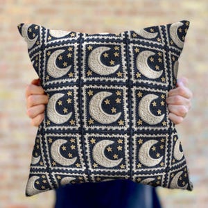 May include: A square throw pillow with a navy blue background and a white crocheted pattern of moons and stars.