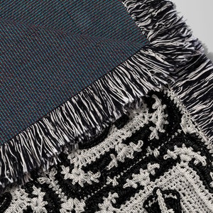 May include: Close-up of a black and white woven throw blanket with a fringe border. The blanket is folded over, revealing a blue and black woven backing.