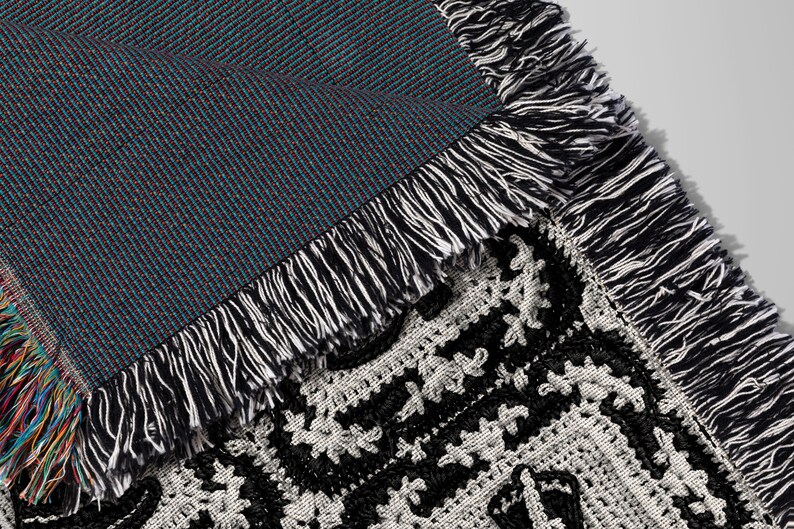 May include: Close-up of a black and white woven throw blanket with a fringe border. The blanket is folded over, revealing a blue and black woven backing.