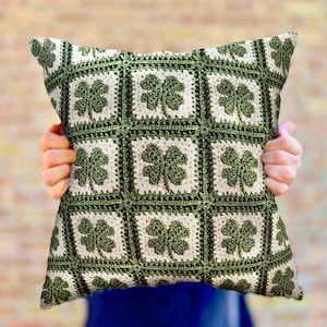 May include: A green and white crocheted pillow with a shamrock pattern. The pillow is made of a soft, textured fabric and has a square shape.