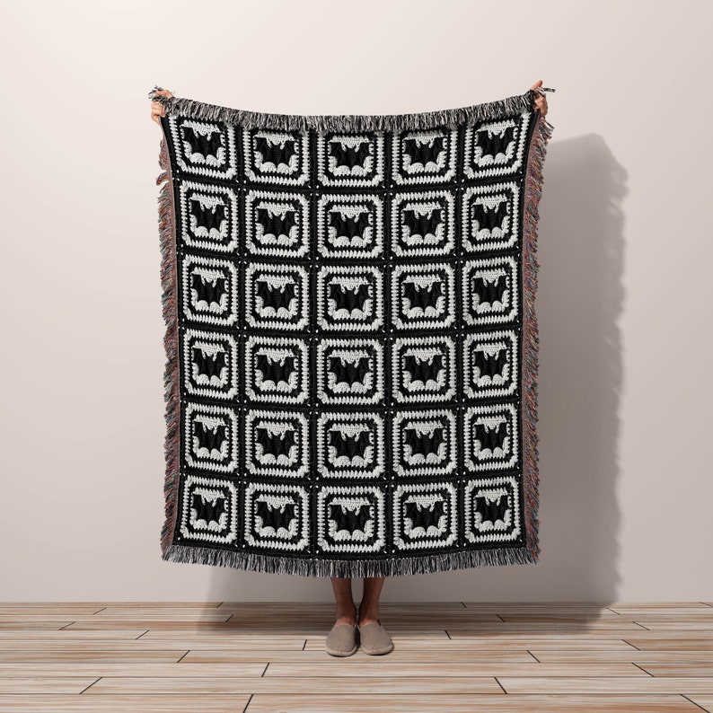 May include: Black and white woven throw blanket with a repeating pattern of bats. The blanket has fringe on all sides.