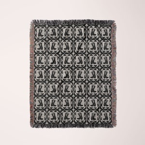 May include: Black and white woven throw blanket with a repeating pattern of cowboy boots in a square frame.