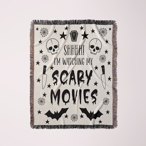 K&ouml;nnte beinhalten: Schwarz-wei&szlig;e gewebte Wolldecke mit einem gruseligen Halloween-Motiv. Sie zeigt einen Sch&auml;del, ein Kreuz, ein Messer, Flederm&auml;use und den Text "Psst! Ich schaue mir meine Horrorfilme an".