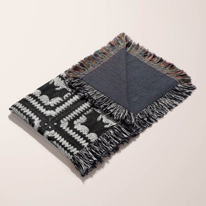 May include: Black and white woven throw blanket with a fringe border. The blanket is folded in half, revealing a solid blue underside.