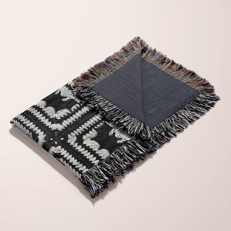 May include: Black and white woven throw blanket with a fringe border. The blanket is folded in half, revealing a solid blue underside.