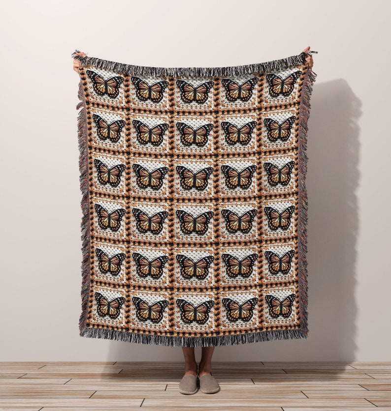 woman standing holding a woven blanket with monarch butterflies in granny square design