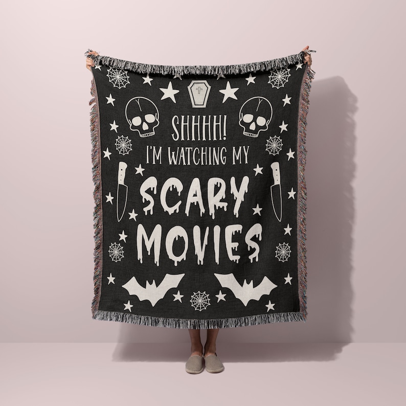 K&ouml;nnte beinhalten: Schwarze und wei&szlig;e gewebte Wolldecke mit einem gruseligen Halloween-Motiv. Sie zeigt einen Totenkopf, Flederm&auml;use, Sterne, Spinnweben und den Text "Psst! Ich schaue mir meine Horrorfilme an".