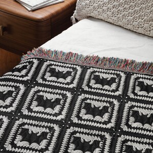 May include: Black and white crocheted throw blanket with a repeating pattern of bats. The blanket has a fringe border with multicolored threads.