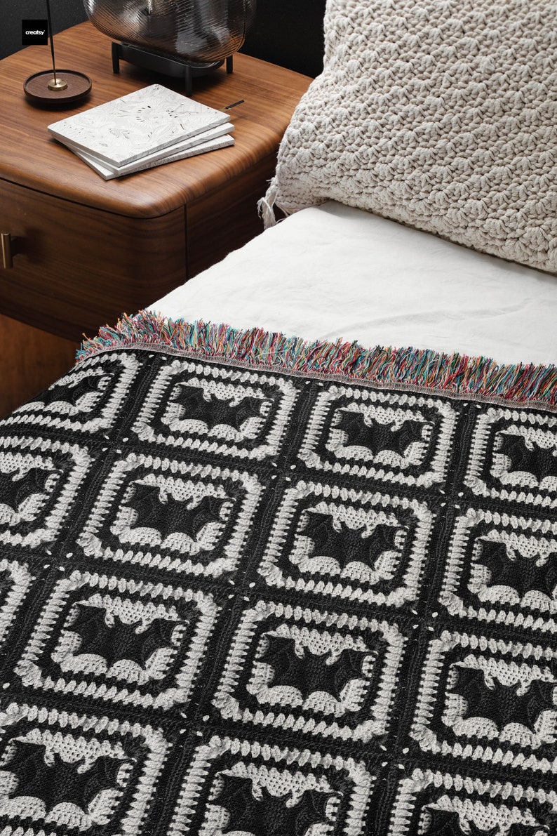 May include: Black and white crocheted throw blanket with a repeating pattern of bats. The blanket has a fringe border with multicolored threads.