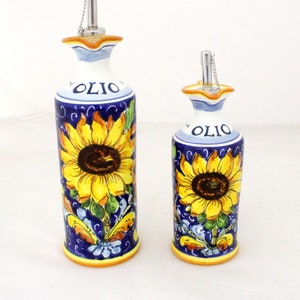 May include: Two ceramic olive oil bottles with sunflower designs. The bottles are blue and white with yellow sunflowers and the word "OLIO" written on them.