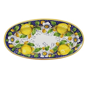 Può includere: Piatto ovale in ceramica con un design dipinto a mano. Il bordo è blu navy con un bordo dorato. Il piatto presenta limoni gialli, fiori bianchi e foglie verdi. Il centro è bianco.