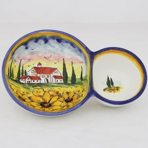 May include: A ceramic serving dish with two connected bowls. The larger bowl features a painted landscape with a farmhouse, sunflowers, and a blue sky. The smaller bowl is white with a yellow and blue rim.