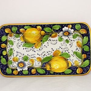 May include: A rectangular ceramic serving tray with a blue and white background. The tray is decorated with a hand-painted design of lemons, flowers, and leaves in shades of yellow, green, and orange.