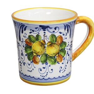Puede incluir: Una taza de cerámica con interior blanco y asa amarilla. El exterior presenta un diseño pintado a mano de fruta amarilla con hojas verdes, espirales azules y un borde amarillo y azul. La taza mide aproximadamente 10 cm de alto.
