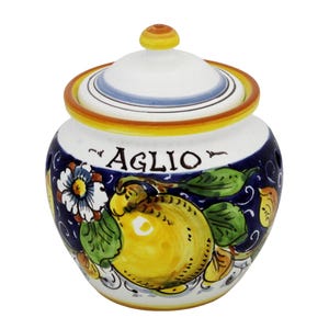 May include: A ceramic garlic jar with a lid. The jar is white with a blue band and a yellow rim. It features a hand-painted design of a yellow lemon, green leaves, and the word "AGLIO".