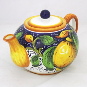 Può includere: Una teiera in ceramica con un design floreale blu e bianco con limoni. La teiera ha un manico giallo e un coperchio bianco con un pomello blu.