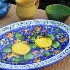 Puede incluir: Una fuente ovalada de cer&aacute;mica con fondo azul y dise&ntilde;o de limones amarillos y verdes. La fuente est&aacute; rodeada de otras piezas de cer&aacute;mica coloridas, incluyendo un cuenco azul con la palabra "FORMAGGIO" y una taza amarilla.