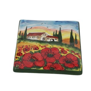 May include: Square ceramic tile featuring a painted landscape with red poppies in the foreground, a farmhouse, and cypress trees under a sunset sky. The tile has a green border and is likely decorative.