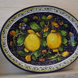 Puede incluir: Plato ovalado de cer&aacute;mica con dise&ntilde;o de limones pintados a mano. El plato presenta un fondo azul oscuro con limones amarillos, hojas verdes y detalles florales. El borde tiene un borde decorativo blanco y amarillo.