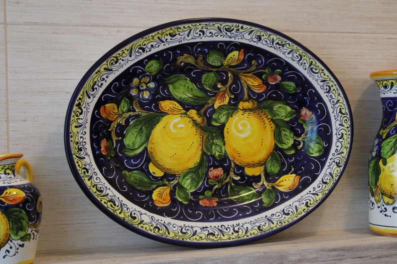 Puede incluir: Plato ovalado de cer&aacute;mica con dise&ntilde;o de limones pintados a mano. El plato presenta un fondo azul oscuro con limones amarillos, hojas verdes y detalles florales. El borde tiene un borde decorativo blanco y amarillo.