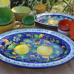 Puede incluir: Una colecci&oacute;n de vajilla de cer&aacute;mica colorida, que incluye fuentes, cuencos y tazas. La fuente ovalada presenta un fondo azul vibrante con un dise&ntilde;o de lim&oacute;n y flores. Otras piezas son amarillas, verdes y naranjas.