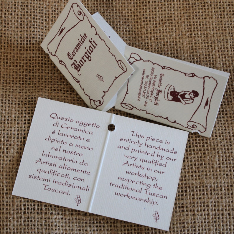 May include: Off-white product tags with burgundy text and illustrations. The tags read "Ceramiche Borgioli" and describe the handmade ceramic pieces, painted by qualified artists in a Tuscan workshop.