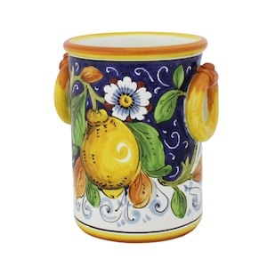 Può includere: Un vaso in ceramica con un design a limoni e fiori. Il vaso presenta uno sfondo blu navy con limoni gialli, foglie verdi e fiori bianchi. Ha due manici gialli e un bordo giallo e arancione.