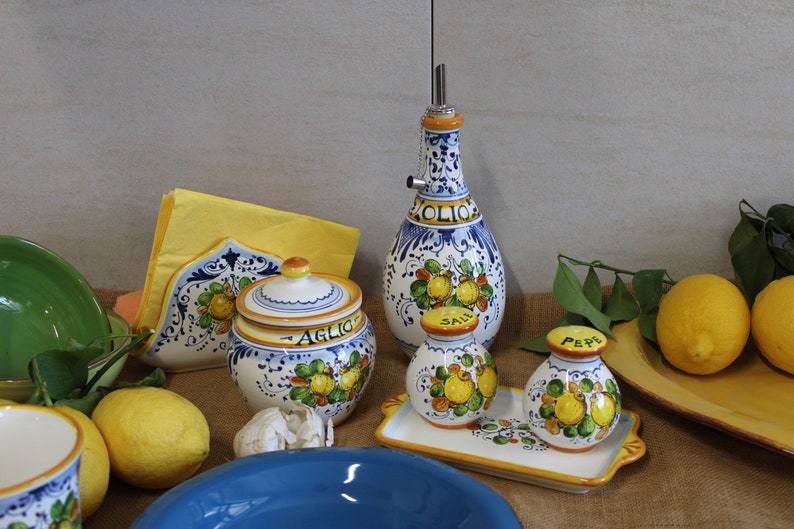 Italian table set, oil cruet, napkinholder, salt and pepper set, garlic jar.The table with a jute tablecloth  is decorated with real lemons and  yellow paper napkin
