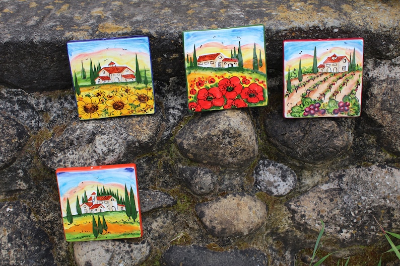 May include: Five square ceramic tiles with hand-painted Italian countryside scenes. Each tile features a different landscape, including sunflowers, poppies, vineyards, and farmhouses, with vibrant colors and a rustic aesthetic.