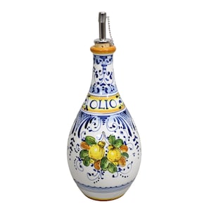 May include: A white ceramic olive oil bottle with a decorative design. The bottle features a blue and white floral pattern, the word "OLIO" in yellow, and a lemon and leaf motif. It has a metal spout and a cork stopper.