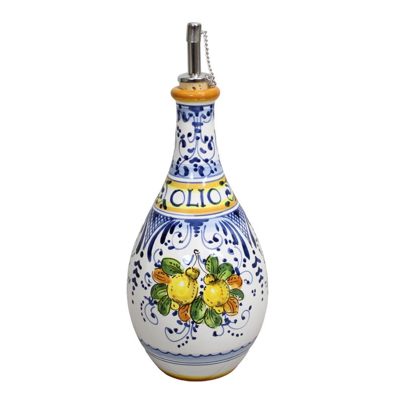 May include: A white ceramic olive oil bottle with a decorative design. The bottle features a blue and white floral pattern, the word "OLIO" in yellow, and a lemon and leaf motif. It has a metal spout and a cork stopper.