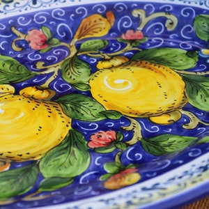 Puede incluir: Plato ovalado de cer&aacute;mica con dise&ntilde;o pintado a mano. El plato presenta un fondo azul vibrante con limones amarillos, hojas verdes y delicados acentos florales en rosa y amarillo. El borde tiene un borde decorativo blanco y azul.