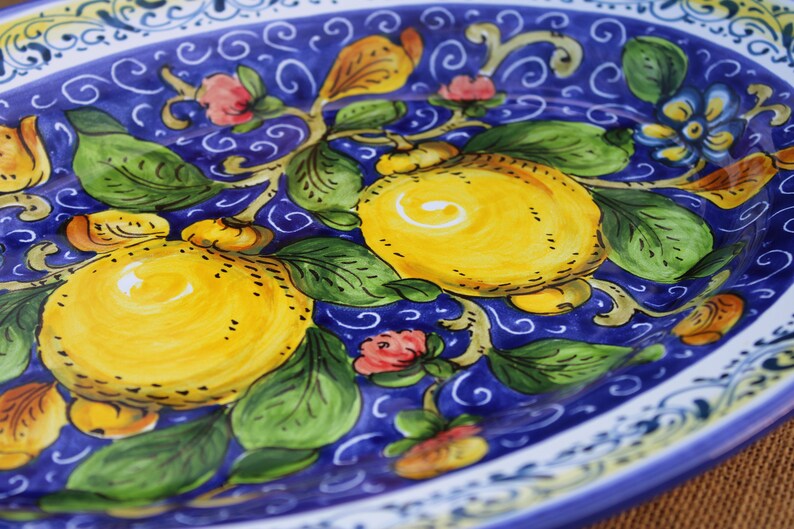Puede incluir: Plato ovalado de cer&aacute;mica con dise&ntilde;o pintado a mano. El plato presenta un fondo azul vibrante con limones amarillos, hojas verdes y delicados acentos florales en rosa y amarillo. El borde tiene un borde decorativo blanco y azul.